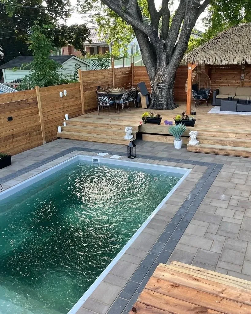 Cour arrière style resort avec piscine creusée, patio en pavé, terrasse en cèdre et abri au toit de chaume