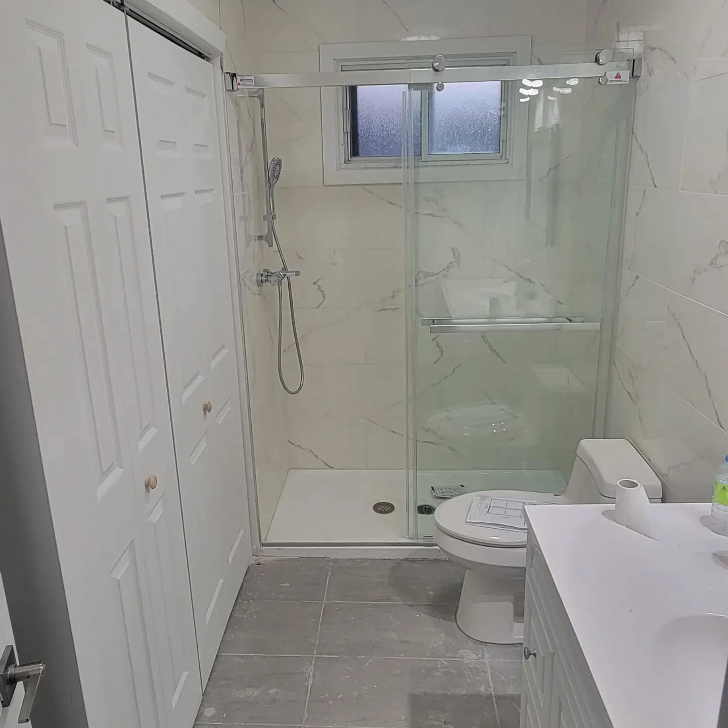 Salle de bain rénovée avec douche en verre et tuile effet marbre, projet avec salle de lavage neuve