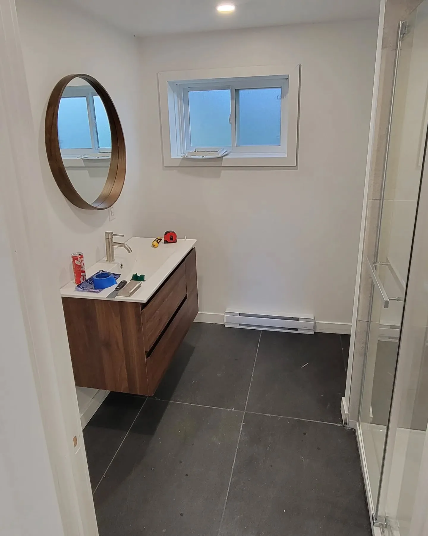Salle de bain modernisée avec meuble-lavabo en noyer, miroir rond et tuile de sol foncée