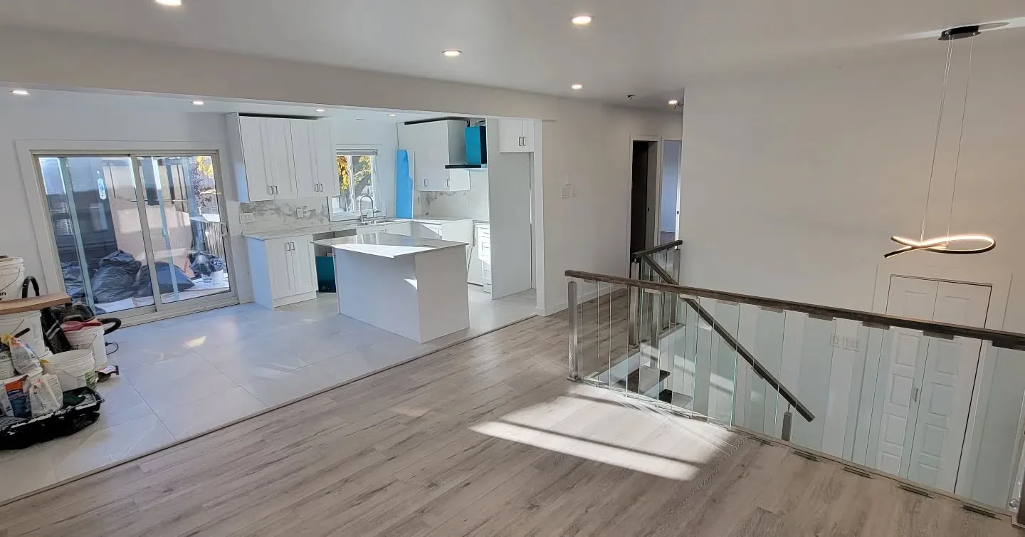 Pièce principale lumineuse d'une rénovation clé en main complète : cuisine blanche ouverte, îlot et escalier à garde-corps de verre