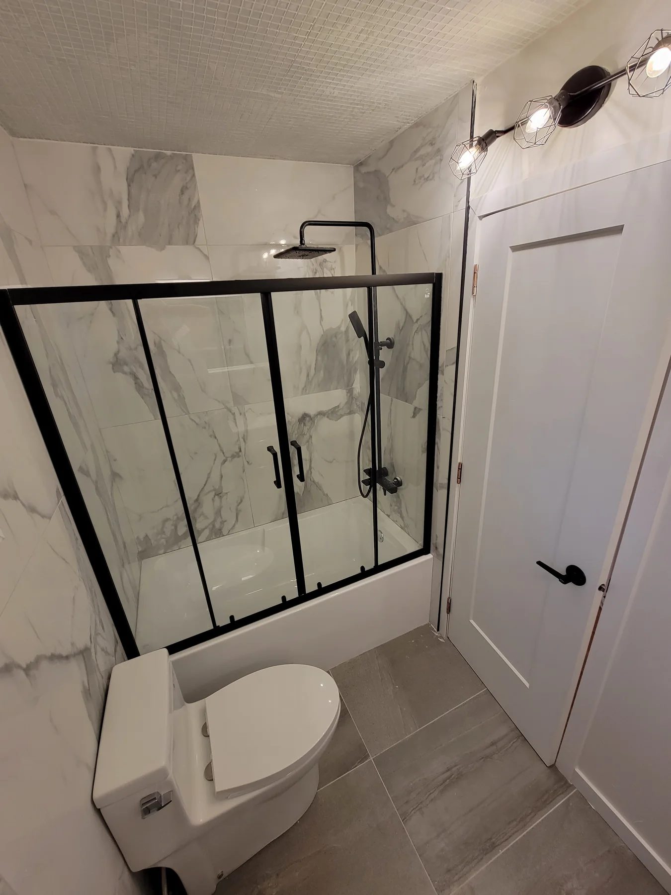 Main bathroom — marble-look tile and a black-framed glass shower