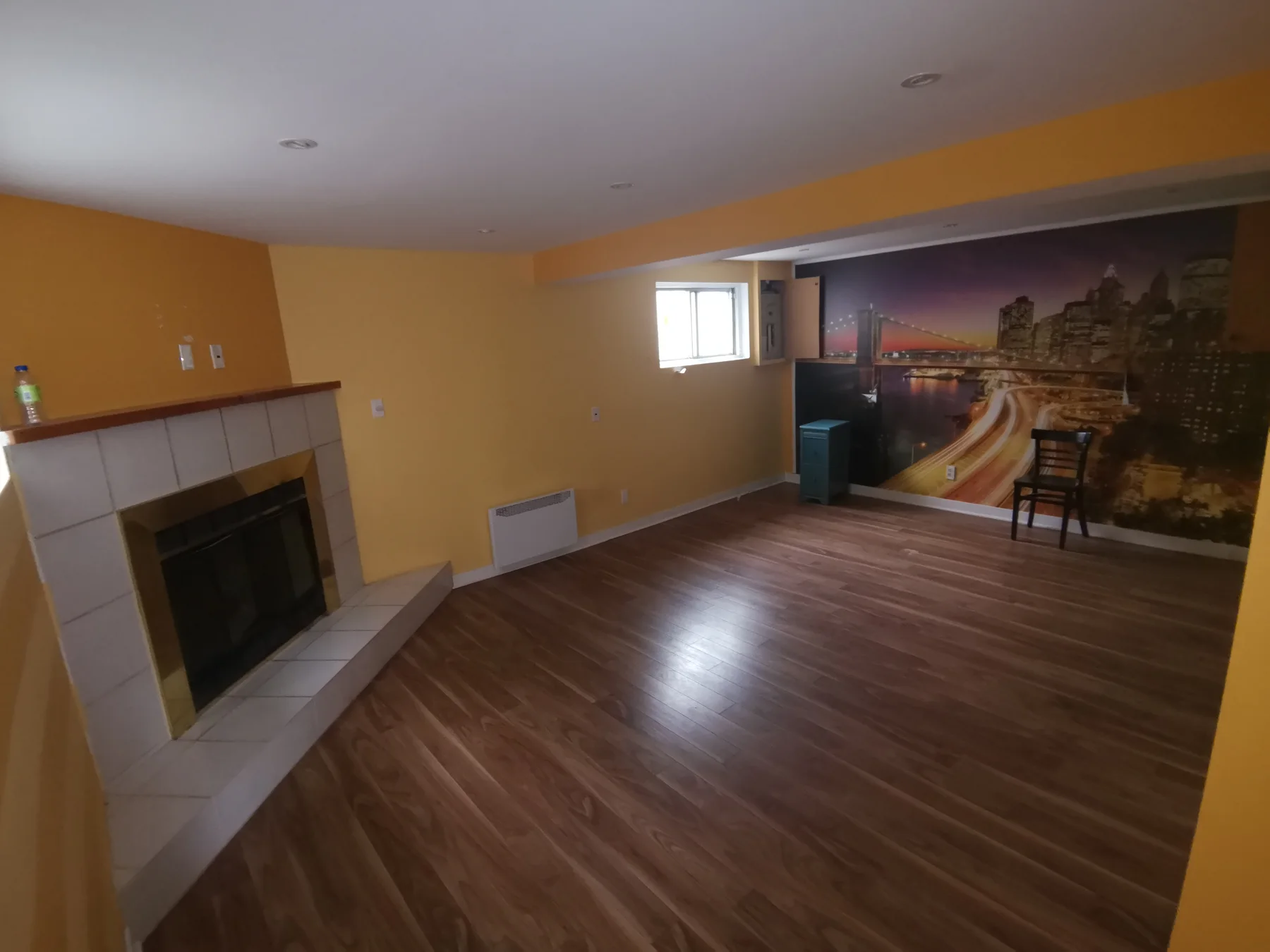 Basement before: mustard walls, tiled fireplace and a city-skyline mural